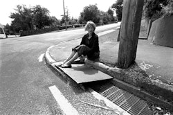 I think perhaps it evokes certain feelings rather than exact memories, but that area around the drain was socially pivotal to us kids. It’s a place where four different roads meet, so it was often a place where you would see your friends. Nearby is the stone bus shelter where we used to sit on the roof and eat lollies. And the drain itself was very exciting when it rained. It had this wonderful rushing sound with all the water running off the hill and coming down from Rapaki Road. It only took a little bit of rain and it would be like this huge flood. You could jump on the iron cover as well, and it would make this great clanging noise. There was another aspect to that drain that I haven’t thought about in a long time. Going past it every day – going to and coming back from school – it was a landmark of sorts. I was a timid wee kid and very unhappy at school. My folks had come out from Britain just before I was born, and when I was five I went to school with an obvious British accent. I didn’t sound like a Kiwi kid at all. I also wore glasses, real wing jobs, and they were pretty ugly. I hated them so much I used to try to hide them or break them. When I was older, in high school, I enjoyed being different, but in my primary school years those sorts of things isolated me. Passing that drain in the mornings meant going somewhere I didn’t want to be. Coming home, the drain was like a gateway. Passing it was very significant: it meant I was nearly home – on the home run – and that represented absolute security.